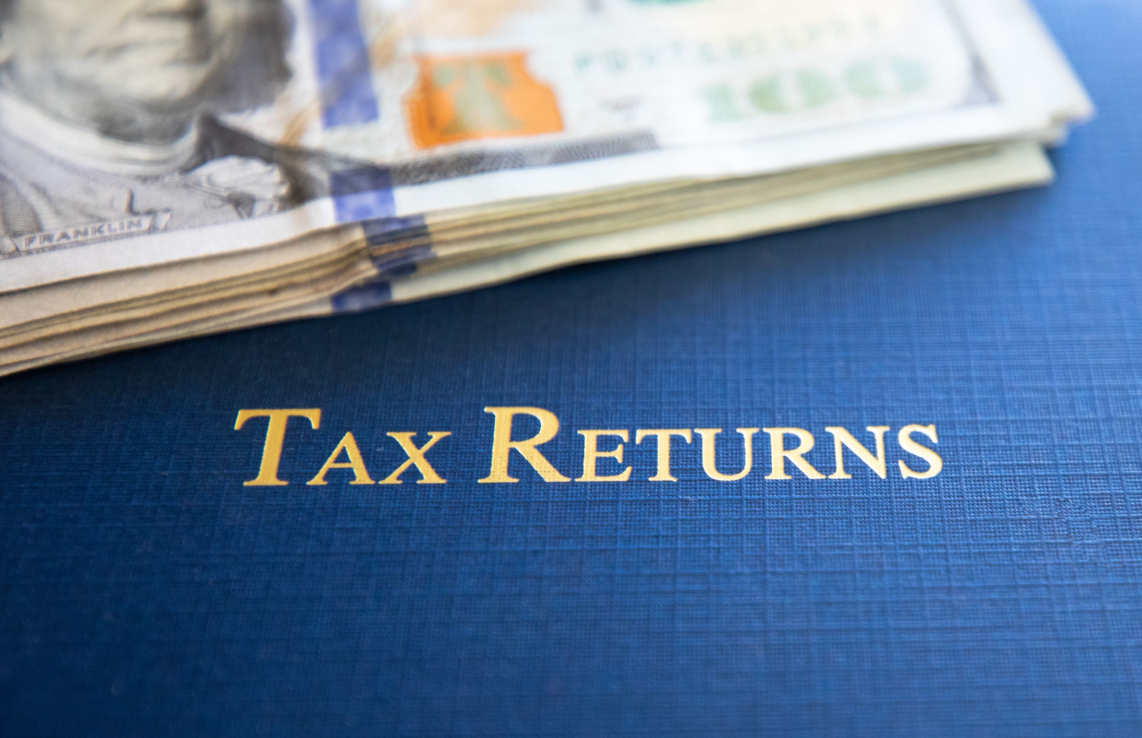 Blue tax returns document folder with gold text and financial documents showing professional tax preparation services